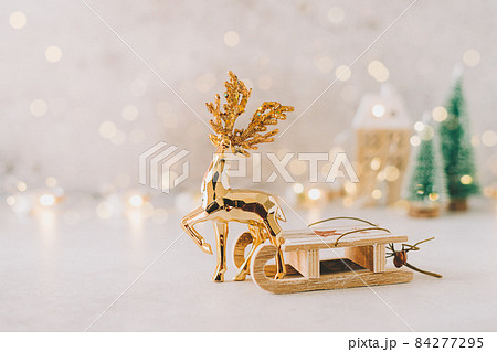 Golden deer dragging eco Natural wooden toy sled on white background with glowing light bokeh, copy space. New year card. Xmas decoration, Christmas tree and wooden house 84277295