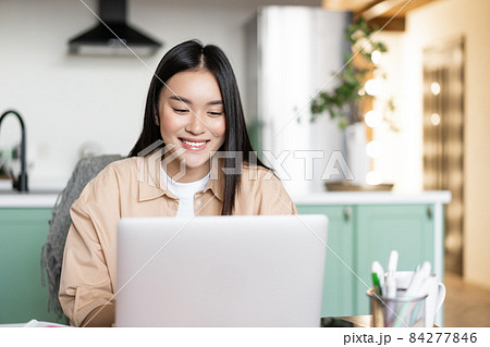 Smiling asian girl using laptop computer, working at home, studying in online school, remote university classes, typing on keyboard Smiling asian girl using laptop computer, working at home, studying in online school, remote university classes, typing on keyboard 84277846