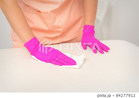 Close up of hands in rubber protective pink gloves cleaning the white surface with a white rag. Close up of hands in rubber protective pink gloves cleaning the white surface with a white rag. 84277912