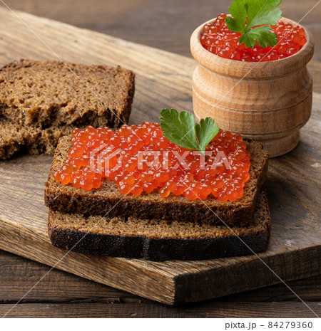 red salmon caviar lies on a piece of rye bread. Brown wooden table 84279360