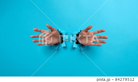 two female palms sticking out of a torn hole in blue paper 84279512