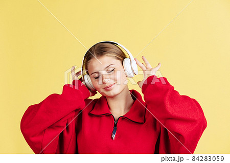 Young smiling beautiful girl listening to music with closed eyes isolated on yellow studio background. Concept of emotions, Young smiling beautiful girl listening to music with closed eyes isolated on yellow studio background. Concept of emotions, 84283059