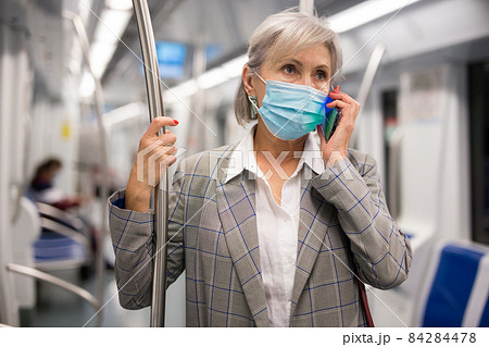 Mature woman in face mask talking on phone inside subway train 84284478