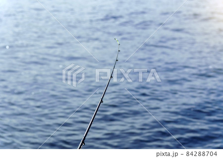 Fishing rod on a background of blue water, selective focus with copy space for text. Fishing rod on a background of blue water, selective focus with copy space for text. 84288704