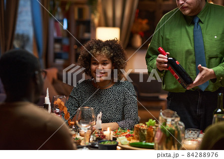 African young woman talking to her friends and smiling while having dinner at the table during a party 84288976