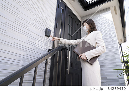 マスクをしてドアの前でインターホンを押す営業の女性 84289450