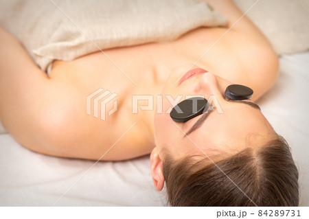 Massage with stones on the eyes of young woman getting a treatment in a beauty spa. 84289731