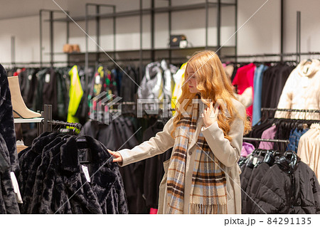 Young female customer with golden hair examining best fur coats 84291135