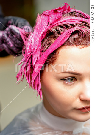 The professional hairdresser uses a brush to apply the pink dye to the hair. Hair coloring concept. 84292203