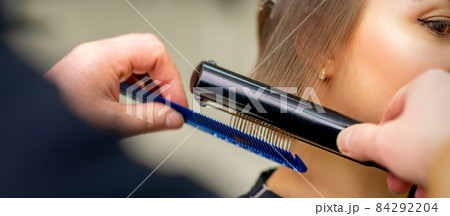A hairdresser is straightening the hair of the young brunette woman in a beauty salon. A hairdresser is straightening the hair of the young brunette woman in a beauty salon. 84292204