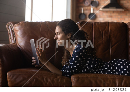 Young latina female lying on belly on couch using tablet 84293321