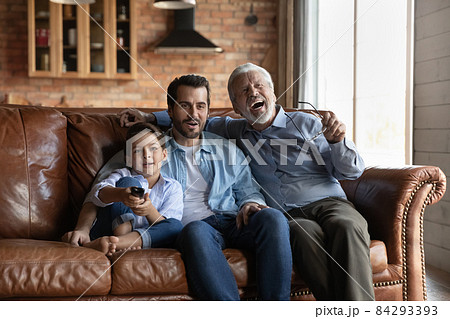 Three male members of multi generational family watching tv together Three male members of multi generational family watching tv together 84293393