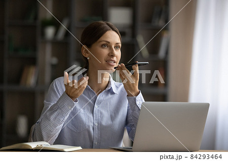 Attractive woman sit at desk holding smartphone talk on speakerphone 84293464