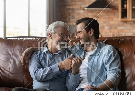 Happy retired dad young son sitting on sofa hugging talking 84293793