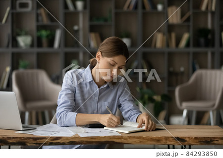 Woman writing in diary, jotting to-do list seated at desk Woman writing in diary, jotting to-do list seated at desk 84293850
