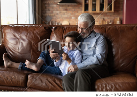Loving elderly grandfather embrace preteen grandkid playing game on touchpad Loving elderly grandfather embrace preteen grandkid playing game on touchpad 84293862