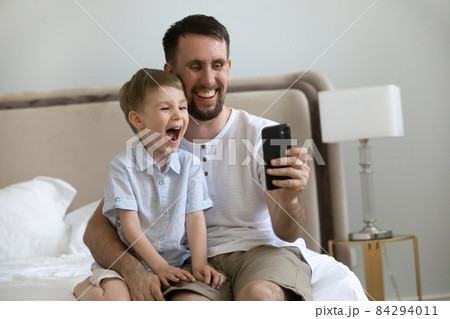 Excited laughing boy and dad using app on mobile phone Excited laughing boy and dad using app on mobile phone 84294011