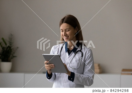 Smiling female doctor therapist using tablet, standing in office room Smiling female doctor therapist using tablet, standing in office room 84294298