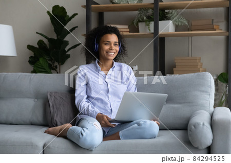 Smiling African American woman in wireless headphones looking in distance Smiling African American woman in wireless headphones looking in distance 84294525