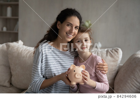 Head shot portrait mother and little daughter holding piggy bank Head shot portrait mother and little daughter holding piggy bank 84294606