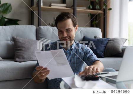 Happy millennial generation man doing domestic financial paperwork. Happy millennial generation man doing domestic financial paperwork. 84294690
