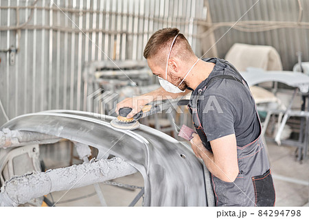 Small Garage. The mechanic works with a grinding tool. Sanding of car elements. Painting car service. Repairing car section after the accident. Small Garage. The mechanic works with a grinding tool. Sanding of car elements. Painting car service. Repairing car section after the accident. 84294798