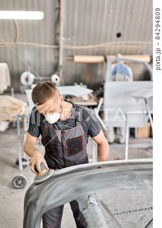 Small Garage. The mechanic works with a grinding tool. Sanding of car elements. Painting car service. Repairing car section after the accident. 84294809