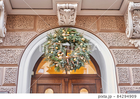 Christmas morning. House with a decorated door with a Christmas wreath and tree branches. Street european city. Christmas morning. House with a decorated door with a Christmas wreath and tree branches. Street european city. 84294909