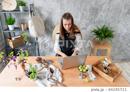 Young female freelancer works on a laptop, responds to messages in social networks. Flower delivery concept. Professional worker in a flower shop. Young female freelancer works on a laptop, responds to messages in social networks. Flower delivery concept. Professional worker in a flower shop. 84295721