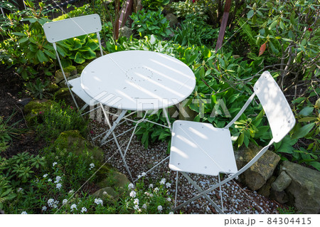 Empty metal bistro coffee table with chairs in green summer garden Empty metal bistro coffee table with chairs in green summer garden 84304415