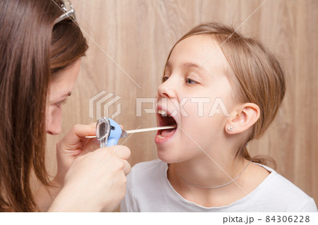 Child check up - doctor examining elementary age girl throat using wooden tongue depressor and torch 84306228