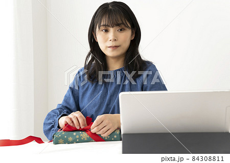 テーブルでリボンのかけ方をネットで検索してみながら結ぶ女性 テーブルでリボンのかけ方をネットで検索してみながら結ぶ女性 84308811
