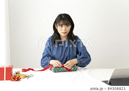 テーブルでプレゼントに赤いリボンをかける女性 84308821