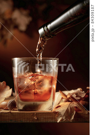 Whiskey is poured into a glass with ice. 84309187