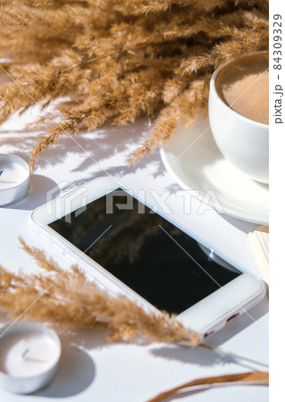 Pampas grass and white cup with coffee. Mobile phone with black screen. Checking social media Drinking Cappuccino in the breakfast morning at home. Flat lay. Wallpaper. Aesthetics Pampas grass and white cup with coffee. Mobile phone with black screen. Checking social media Drinking Cappuccino in the breakfast morning at home. Flat lay. Wallpaper. Aesthetics 84309329