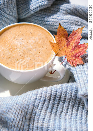 White cup of morning warming coffee on blue knitted sweater with maple yellow leaves background. Cozy home concept. Aesthetics blog lifestyle. Autumn Still life. Cappuccino or latte hot drink 84309330