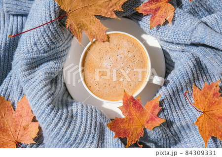 White cup of morning warming coffee on blue knitted sweater with maple yellow leaves background. Cozy home concept. Aesthetics blog lifestyle. Autumn Still life. Cappuccino or latte hot drink White cup of morning warming coffee on blue knitted sweater with maple yellow leaves background. Cozy home concept. Aesthetics blog lifestyle. Autumn Still life. Cappuccino or latte hot drink 84309331