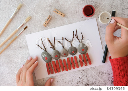 Diy Merry Christmas deer on greeting card postcard made of pebbles, sea stones, clothespins and branches on white background. Natural Eco style diy. Gift idea. Step by step. Top view. 84309366