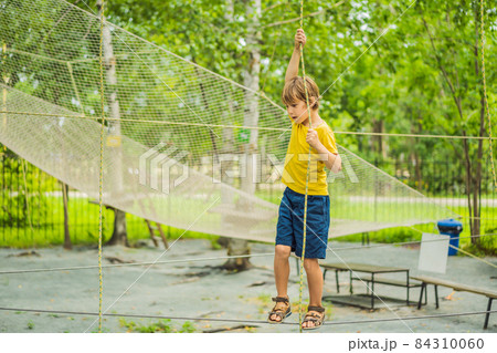 Little boy in a rope park. Active physical recreation of the child in the fresh air in the park. Training for children Little boy in a rope park. Active physical recreation of the child in the fresh air in the park. Training for children 84310060