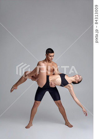 The couple of a young modern ballet dancers in black suits are posing over a gray studio background. 84313009