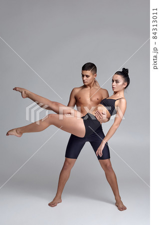 The couple of a young modern ballet dancers in black suits are posing over a gray studio background. The couple of a young modern ballet dancers in black suits are posing over a gray studio background. 84313011