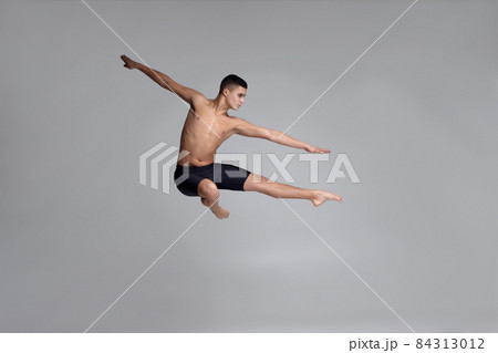 Photo of a handsome man ballet dancer, dressed in a black shorts, making a dance element against a gray background in studio. Photo of a handsome man ballet dancer, dressed in a black shorts, making a dance element against a gray background in studio. 84313012