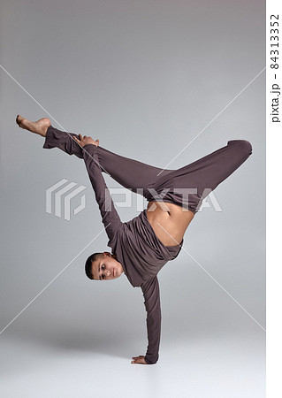 Photo of an athletic man ballet dancer dressed in a gray tracksuit, making a dance element against a gray background in studio. Photo of an athletic man ballet dancer dressed in a gray tracksuit, making a dance element against a gray background in studio. 84313352