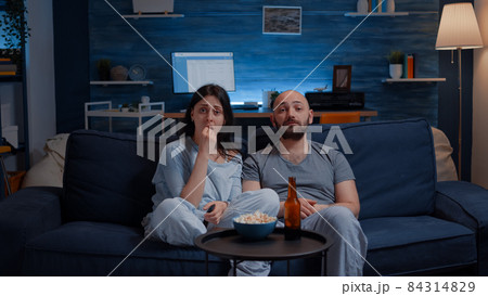 Amazed couple watching movie on TV at night and eating popcorn Amazed couple watching movie on TV at night and eating popcorn 84314829