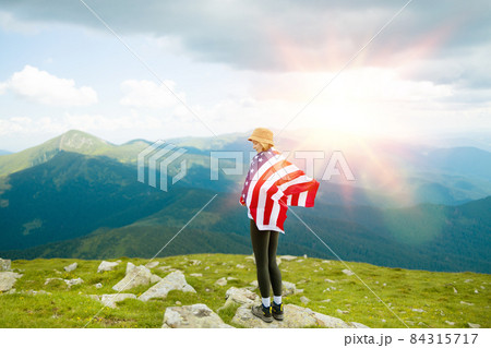 Female is waving American flag on top of mountain at sky background, celebrating independence day Female is waving American flag on top of mountain at sky background, celebrating independence day 84315717