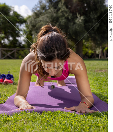 Young concentrated woman in plank position on mat in a park in a summer day 84315740