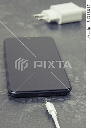 Black smartphone and unconnected cable of charger. Telephone charging Black smartphone and unconnected cable of charger. Telephone charging 84318017