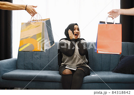 Arabic woman in headscarf sitting on a sofa with packages. Girl did online shopping 84318642