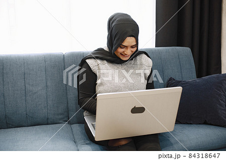 Arabic woman in headscarf using laptop at home, paying for utilities online. Arabic woman in headscarf using laptop at home, paying for utilities online. 84318647