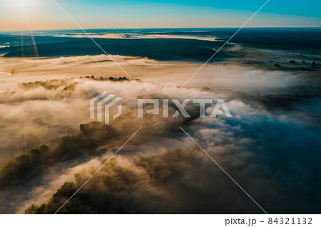 Aerial  view of a beautiful summer  landscape with a fog while dawn.  Photo from drone of a foggy landscape in spring. Top view to land while sunrise. Early morning in nature, misty  weather. 84321132
